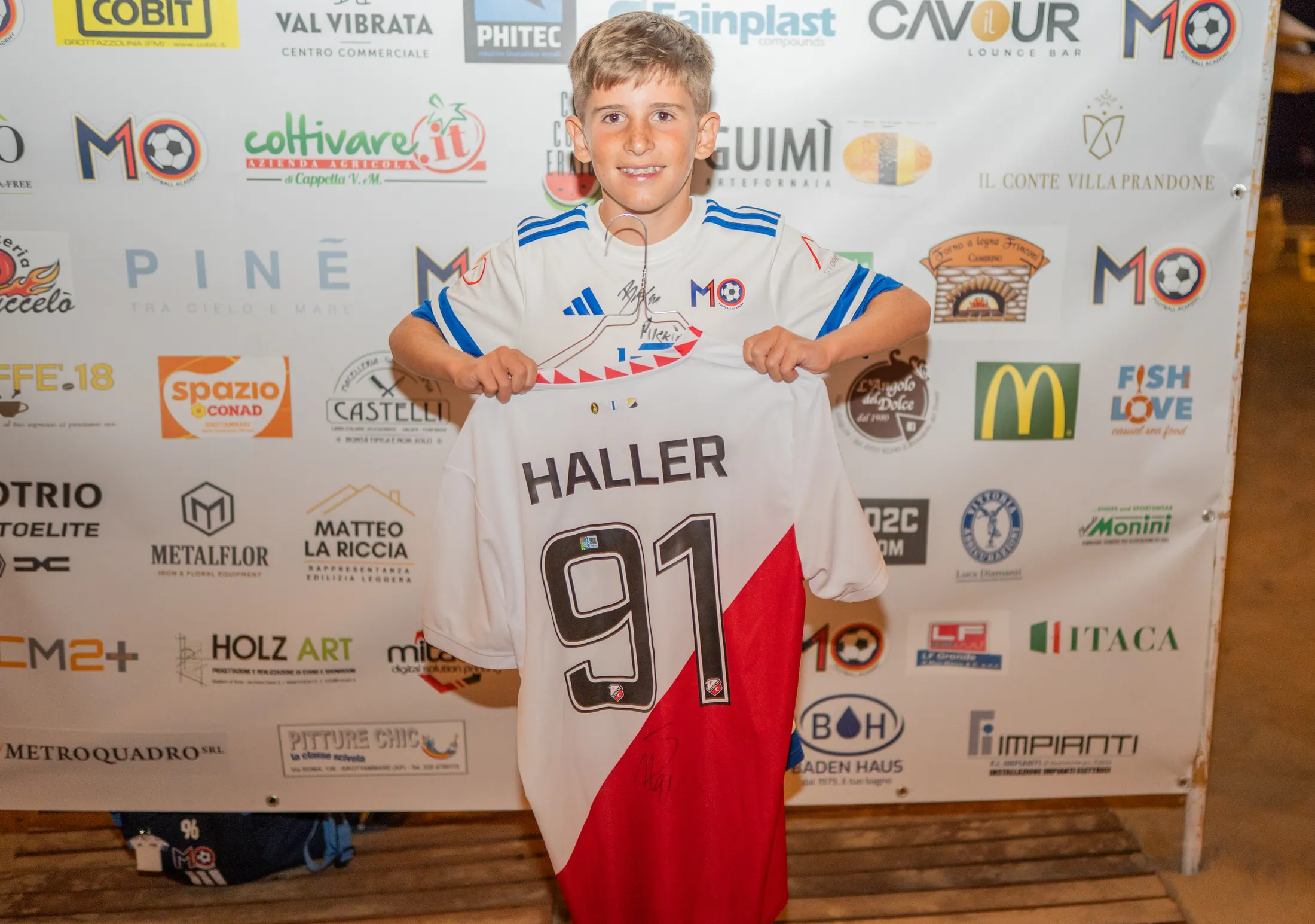Maglia premio consegnata davanti al muro degli sponsor del camp 2026